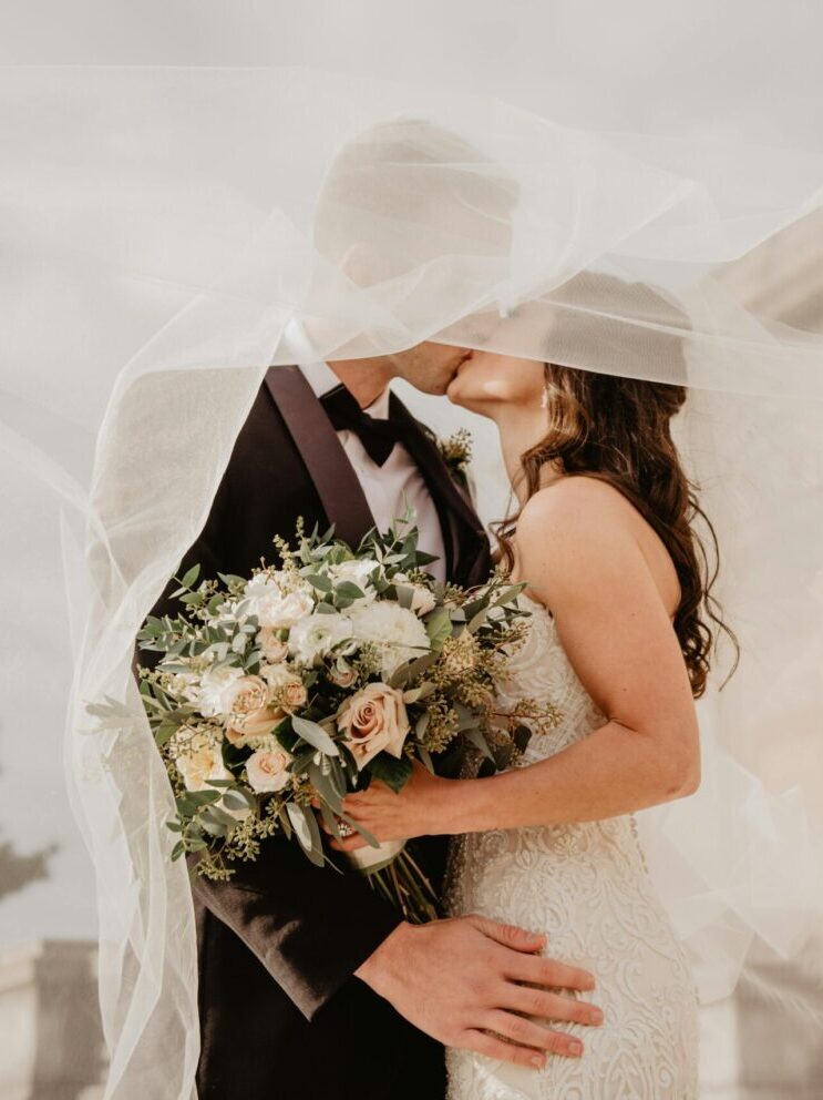 Bride and groom share a tender kiss under a veil, showcasing love and romance on their special day.