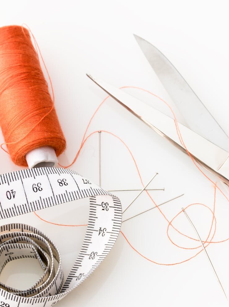 Photo of sewing essentials: scissors, thread, needles, and tape measure on a white background.