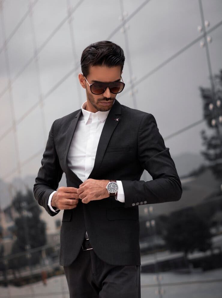 A fashionable man in a black suit adjusting his jacket outdoors in Dubai.